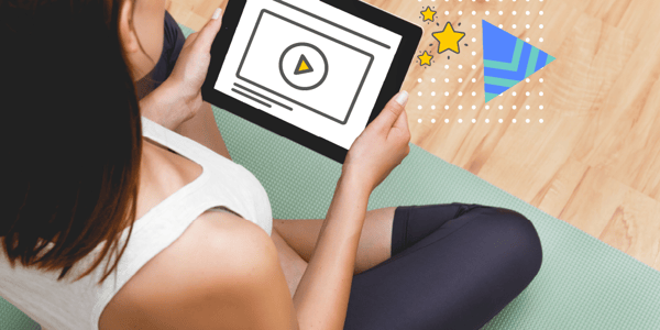 woman in workout clothes sitting on a yoga mat watching a workout video